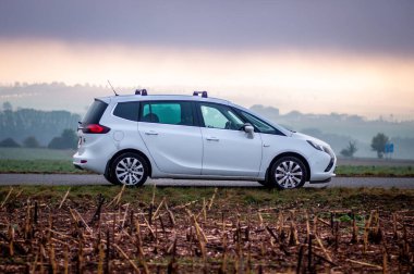 Beyaz aile MPV arabası Opel Zafira sonbaharda siste bir sahada duruyor.