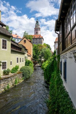 Cesky Krumlov, Çek Cumhuriyeti. Eski evlerin arasında akan nehir olan dar bir sokak. Arka planda yüksek kulesi olan bir kale..