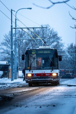 Brno, Çek Cumhuriyeti - 2 Aralık 2023: Bir şehir toplu taşıma otobüsü kışın karlı bir yolda gece yarısı yanan bir sokakta sürüyor.