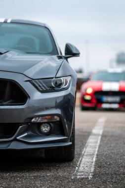 Brno, Çek Cumhuriyeti - 31 Aralık 2023: Otoparkta gri bir Ford Mustang 'in farına yakın çekim. Arkasında hızlı kırmızı bir spor araba daha var..