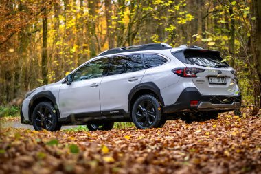 Brno, Çek Cumhuriyeti - 10 Kasım 2023: Beyaz Subaru Outback SUV yapraklarla dolu bir sonbahar ormanında doğada duruyor.