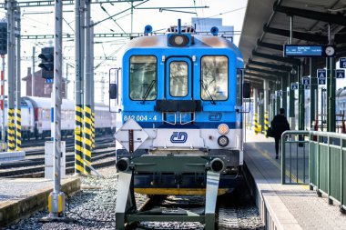 Brno, Çek Cumhuriyeti - 18 Mart 2024: Platformun yanındaki tren istasyonunda mavi beyaz bir lokomotif duruyor. Şehirdeki bir istasyonda yolcu bekleyen bir tren..