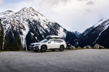 Krimmml, Avusturya - 30 Mart 2024: Beyaz Subaru Outback arazi aracı Alplerdeki karlı dağların altında bir yol gezisinde.