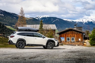 Krimmml, Avusturya - 30 Mart 2024: Beyaz Subaru Outback off-road otomobili Ap 'te eski bir ahşap kulübenin yanında kayak için bir kutu.