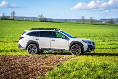 Brno, Çek Cumhuriyeti - 10 Nisan 2024: Beyaz Subaru Outback SUV, ilkbahar tarlasında yeşil çimenli açık hava yolu.