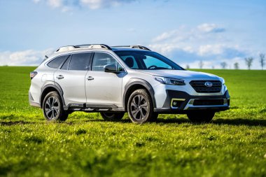 Brno, Çek Cumhuriyeti - 10 Nisan 2024: Beyaz Subaru Outback SUV, ilkbahar tarlasında yeşil çimenli açık hava yolu.