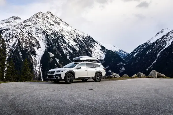 Krimmml, Avusturya - 30 Mart 2024: Beyaz Subaru Outback arazi aracı Alplerdeki karlı dağların altında bir yol gezisinde.