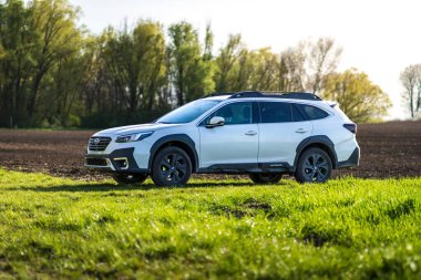 Brno, Çek Cumhuriyeti - 10 Nisan 2024: Beyaz Subaru Outback SUV, ilkbahar tarlasında yeşil çimenli açık hava yolu.