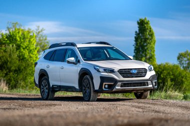 Brno, Çek Cumhuriyeti - 25 Nisan 2024: Japonya 'da yapılmış beyaz bir Subaru Outback arazi aracı doğadaki bir toprak yolda duruyor. Beyaz aile SUV ön görünümü.