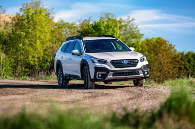 Brno, Çek Cumhuriyeti - 25 Nisan 2024: Japonya 'da yapılmış beyaz bir Subaru Outback arazi aracı doğadaki bir toprak yolda duruyor. Beyaz aile SUV ön görünümü.