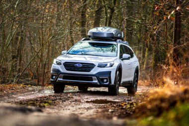 Brno, Çek Cumhuriyeti - 25 Nisan 2024: Ormandaki çamurlu bir yolda kayak kutulu beyaz Subaru Outback arabası. Kırık bir yolda dört çeker geniş bir SUV..