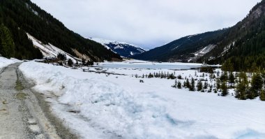 Avusturya 'da Knigsleiten yakınlarında bir dağ gölü. Karlı yol ve Alplerdeki donmuş göl.