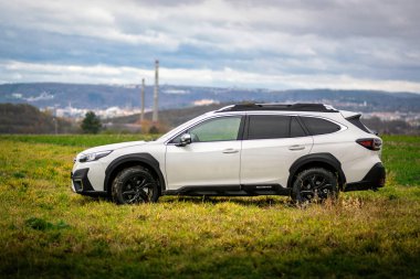 Brno, Çek Cumhuriyeti - 20 Kasım 2024: Sonbaharda açık havada beyaz SUV Subaru Outback, arka planda şehir olan bir arazide.