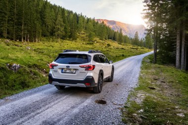 Schladming, Avusturya - 25 Ağustos 2024: Akşamüstü dağlarda gün batımında beyaz aile SUV Subaru Outback. Dağlar arasında Alpler 'deki off-road arabası..