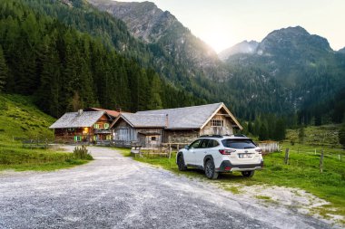 Schladming, Avusturya - 25 Ağustos 2024: Akşamüstü dağlarda gün batımında beyaz aile SUV Subaru Outback. Dağlar arasında Alpler 'deki off-road arabası..