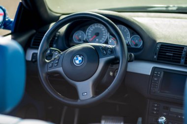 Brno, Czech Republic - October 15, 2024: Interior of an older BMW M3 car, detail of the steering wheel and dashboard controls and buttons. clipart