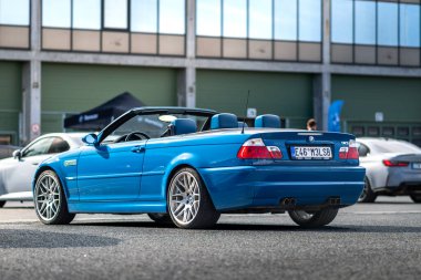 Brno, Çek Cumhuriyeti - 15 Ekim 2024: Mavi spor araba BMW M3 Cabrio asfalt bir otoparkın önünde duruyor. Alman hızlı premium arabası.