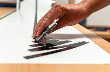 Bir adamın eli iş başında, elinde malayla kesilmiş folyoyla reklam etiketleri yapıyor..