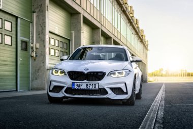 Brno, Çek Cumhuriyeti - 15 Ekim 2024: Beyaz spor BMW M2 bir garaj evinin önündeki yolda. Otoparktaki hızlı Alman arabası..