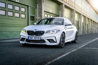 Brno, Çek Cumhuriyeti - 15 Ekim 2024: Beyaz spor BMW M2 bir garaj evinin önündeki yolda. Otoparktaki hızlı Alman arabası..