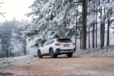 Brno, Çek Cumhuriyeti - 5 Ocak 2024: Kış mevsiminde donmuş ağaçlarla kaplı bir ormanda aile SUV Subaru Outback. Beyaz off-road arabası dışarıda, ağaçların arasında donuyor..