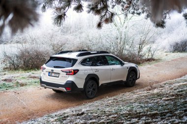 Brno, Çek Cumhuriyeti - 5 Ocak 2024: Kış mevsiminde donmuş ağaçlarla kaplı bir ormanda aile SUV Subaru Outback. Beyaz off-road arabası dışarıda, ağaçların arasında donuyor..