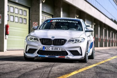 Brno, Çek Cumhuriyeti - 22 Ekim 2024: Hızlı BMW M2 spor arabası yolda. Yarış pistinde garajların önünde yarış arabası..