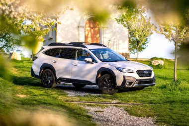 Güney Moravya, Çek Cumhuriyeti - 5 Mayıs 2024: Beyaz modern Subaru Outback SUV, baharda çiçek açan ağaçların yanındaki bir çayırda duruyor. Ailenin dört çeker off-road arabası..