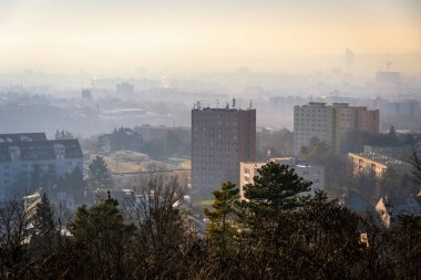Brno, Çek Cumhuriyeti - 10 Ocak 2025: Gün batımında şehrin bulutlu ve sisli manzarası. Şehrin üzerindeki gökyüzü güneş ışığıyla yıkanır ve evler kış havasının tersine döndüğünde puslu olur..