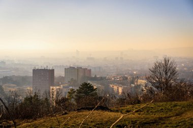 Brno, Çek Cumhuriyeti - 10 Ocak 2025: Gün batımında şehrin bulutlu ve sisli manzarası. Şehrin üzerindeki gökyüzü güneş ışığıyla yıkanır ve evler kış havasının tersine döndüğünde puslu olur..