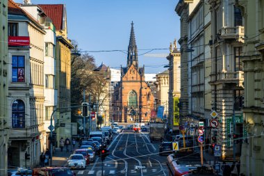 Brno, Çek Cumhuriyeti - 20 Aralık 2024: Brno şehir merkezinde bir sürü insan, araba ve tramvay bulunan ana cadde. Eski binalar ve kırmızı tuğlalı kilise.