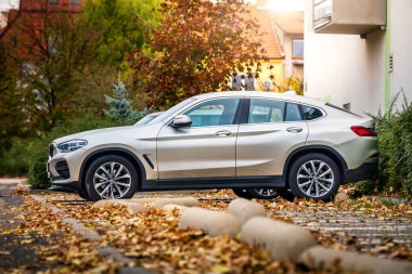 Güney Moravya, Çek Cumhuriyeti - 15 Kasım 2024: Lüks SUV BMW X6 sonbaharda bir apartmanın önünde caddeye park edilmiş. Sokakta düşen yapraklar ve arka planda güneş.