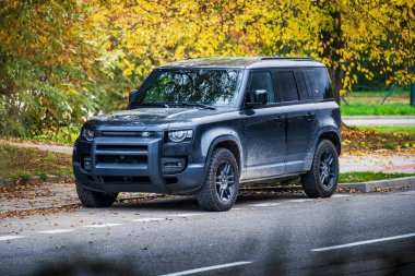 Güney Moravya, Çek Cumhuriyeti - 10 Kasım 2024: Black Land Rover Defender 110 off-road car Sonbaharda bir ağacın altına park edildi.