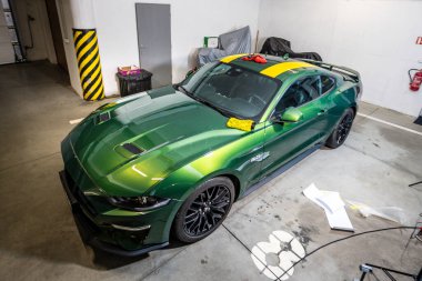 Brno, Çek Cumhuriyeti - 5 Mayıs 2025: Sarı vinil filmden yapılmış hız şeritlerinin montajı sırasında garajda yeşil Ford Mustang. Hızlı bir spor arabaya tasarım çıkartması yapıştırmak.