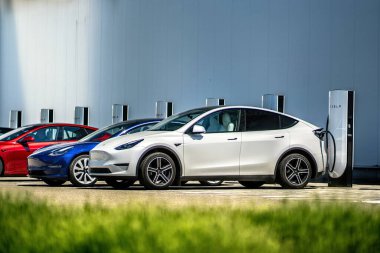 Brno, Çek Cumhuriyeti - 13 Mayıs 2025: Beyaz elektrikli araba Tesla Y bir şarj istasyonuna kabloyla bağlanır ve bir sonraki sefer için aküyü şarj eder. Halka açık bir şarjörde arabayı şarj etmek..
