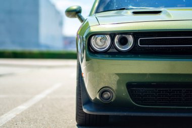 Brno, Çek Cumhuriyeti - 18 Mayıs 2025: Yeşil Amerikan Coupe Dodge Challenger açık havada ağaçların altındaki bir otoparkta park edilmiş. Ön ışıkların ayrıntıları..