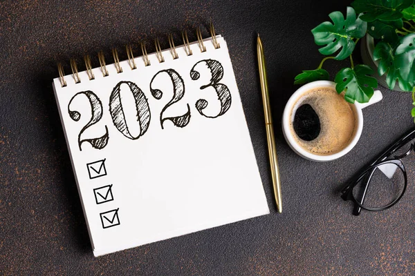 New year resolutions 2023 on desk. 2023 resolutions list with notebook, coffee cup on table. Goals, resolutions, plan, action, checklist concept. New Year 2023 background. Copy spac