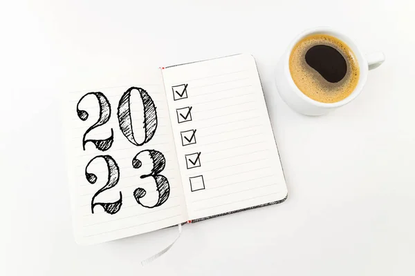 New year resolutions 2023 on white desk. 2023 resolutions list with notebook, coffee cup on table. Goals, resolutions, plan, action, checklist concept. New Year 2023 template, copy spac