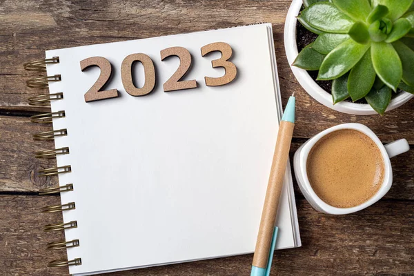New year resolutions 2023 on desk. Wooden eco friendly reusable new year decorations 2023, notebook, coffee cup on table. Goals, resolutions, plan, sustainable concept. New Year 2023 holiday