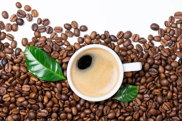 Cup of coffee with foam, delicious aroma coffee. Coffee cup and leaves on coffee beans background. Top view. Copy space