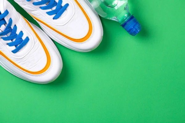 Sport shoes and sport equipment for fitness healthy lifestyle, exercise, health concept. Sport background with shoes and water bottle on green. Copy space