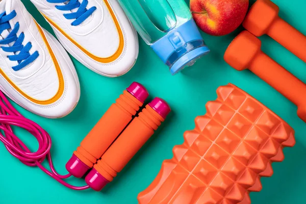 Sport shoes and equipment for fitness healthy lifestyle, exercise, healthy food concept. Sport background with sport equipment shoes, dumbbells, jumping rope, fruit and water bottle on blue background