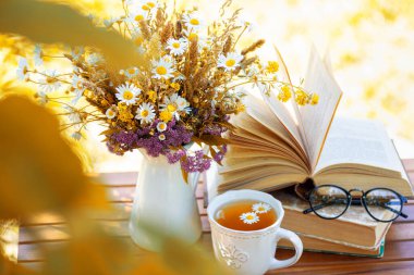 Bouquet of flowers, croissant, cup of tea or coffee, books on table in autumn garden. Rest in garden, reading books, breakfast, vacations in nature concept. Autumn time in garden on backyard