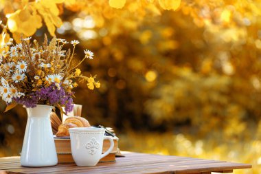 Bouquet of flowers, croissant, cup of tea or coffee, books on table in autumn garden. Rest in garden, reading books, breakfast, vacations in nature concept. Autumn time in garden on backyard