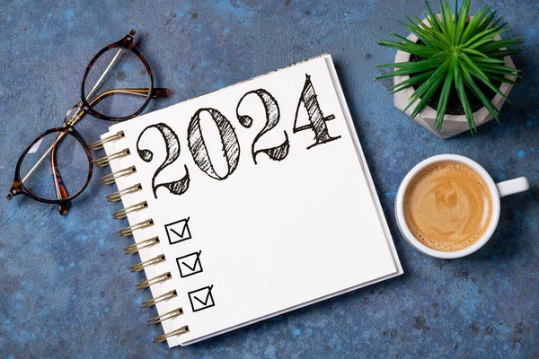 New year resolutions 2024 on desk. 2024 goals list with notebook, coffee cup, plant on wooden table. Resolutions, plan, goals, action, checklist, idea concept. New Year 2024 resolutions, copy space