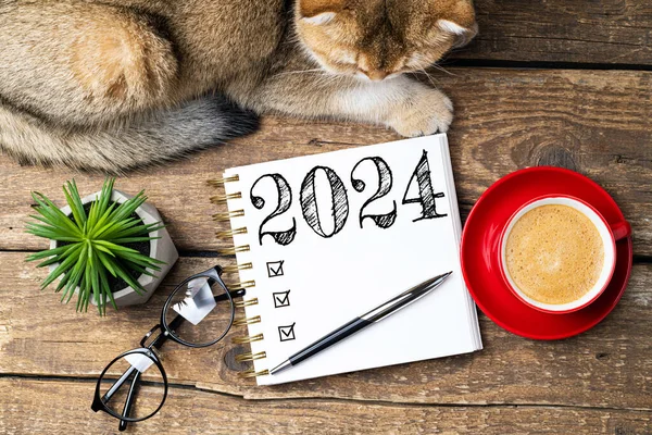 新年の決議2024が机の上に ノートブック コーヒーカップ テーブルにかわいい猫が付いている2024決議リスト 居心地の良い衛生コンセプト 新年2024テンプレート コピースペース — ストック写真