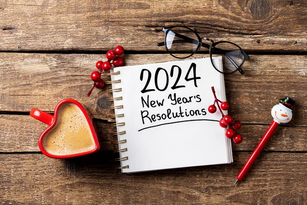 New year resolutions 2024 on desk. 2024 goals list with notebook, coffee cup on wooden table. Resolutions, plan, goals, action, checklist, idea concept. New Year 2024 resolutions, copy space