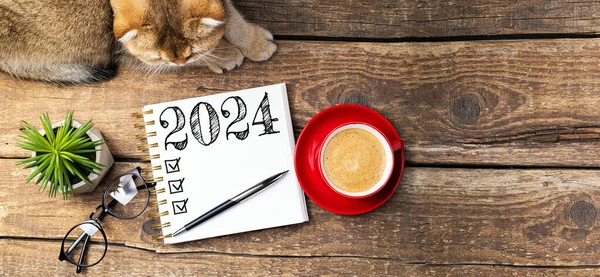 新年の決議2024が机の上に ノートブック コーヒーカップ テーブルにかわいい猫が付いている2024決議リスト 居心地の良い衛生コンセプト 新年2024テンプレート コピースペース — ストック写真