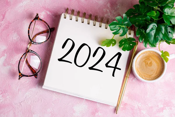 New year resolutions 2024 on desk. 2024 resolutions list with notebook, coffee cup on pink table. Goals, resolutions, plan, action, checklist concept. New Year 2024 template, copy space
