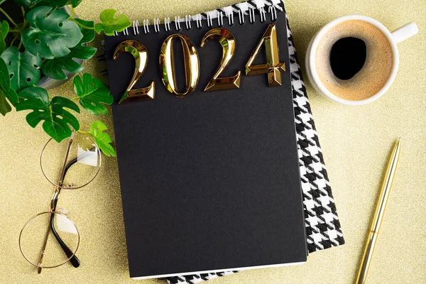 New year resolutions 2024 on desk. 2024 goals list with notebook, coffee cup, plant on golden background. Resolutions, plan, goals, action, checklist, idea concept. New Year 2024 resolutions. Copy space